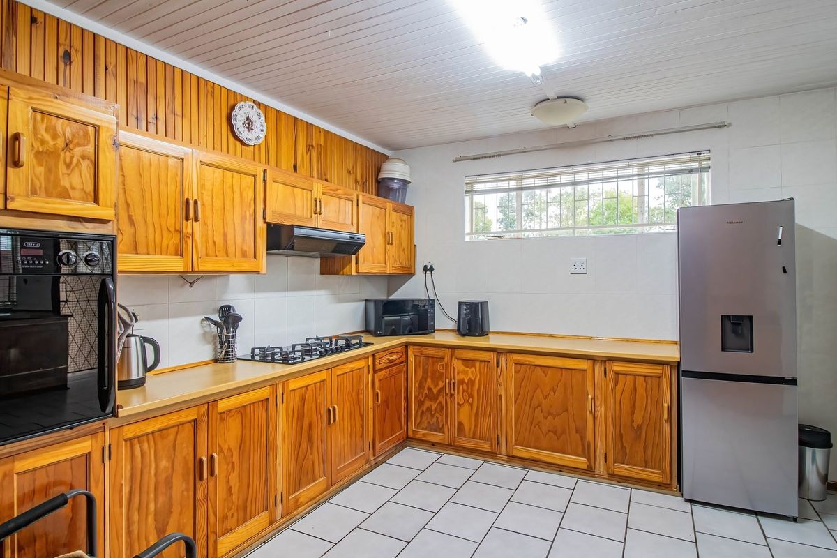 A functional kitchen featuring extensive wooden cabinetry, a built-in oven, gas hob, extractor fan, and tiled flooring with a neutral splashback.