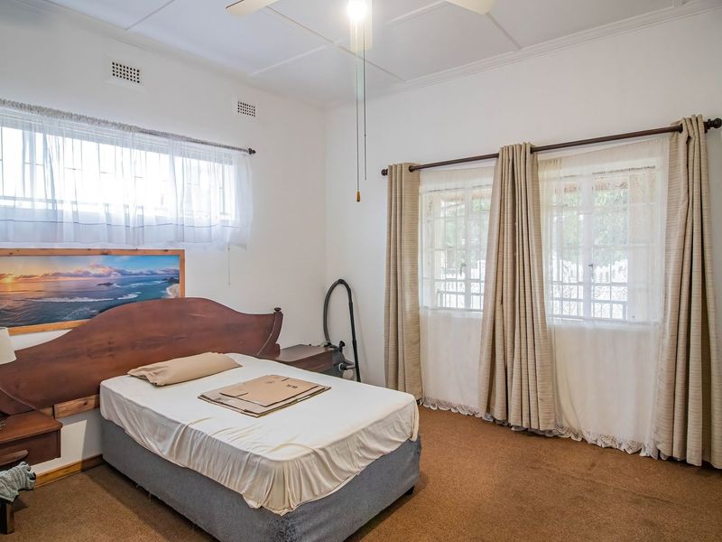 A spacious bedroom featuring built-in cupboards, a ceiling fan, and security bars on the windows, offering a functional and well-lit living space.