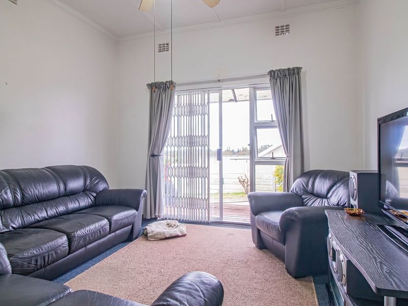 A comfortable living room featuring a ceiling fan, cornice detailing, and a sliding glass door with a security gate leading to the exterior.