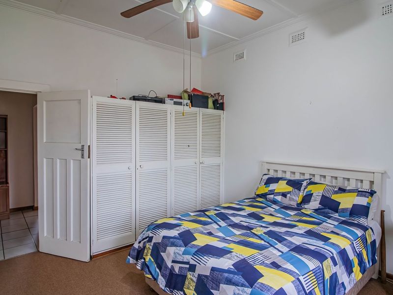 A bedroom featuring built-in louvered wardrobes, a ceiling fan, and neutral wall finishes, offering a functional space with potential for modern updates.