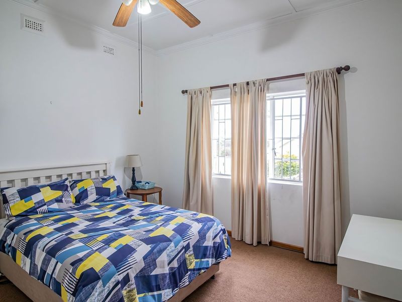 A functional bedroom featuring carpeted flooring, a ceiling fan, and windows fitted with security bars.