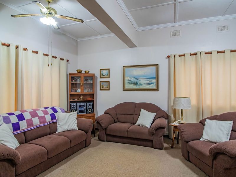 A comfortable living room featuring a coffered ceiling, ceiling fan, and neutral wall finishes, providing a functional and well-maintained space for relaxation.