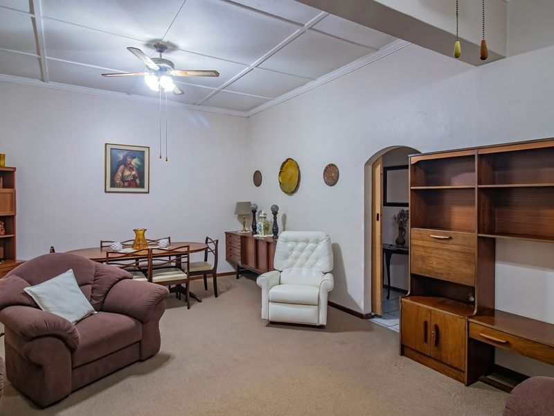 A spacious living room featuring carpeted flooring, a ceiling fan, and a classic arched doorway leading to an adjacent area.