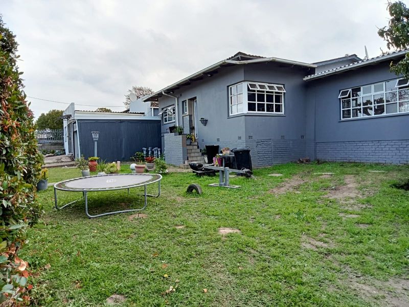 Rear view of the property featuring a painted brick exterior, casement windows, and a spacious backyard area with a detached metal garage structure.