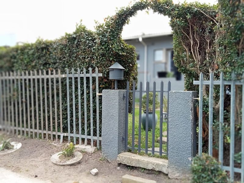 Front entrance view featuring a metal picket fence, pedestrian gate with concrete pillars, and established hedging providing privacy to the property frontage.