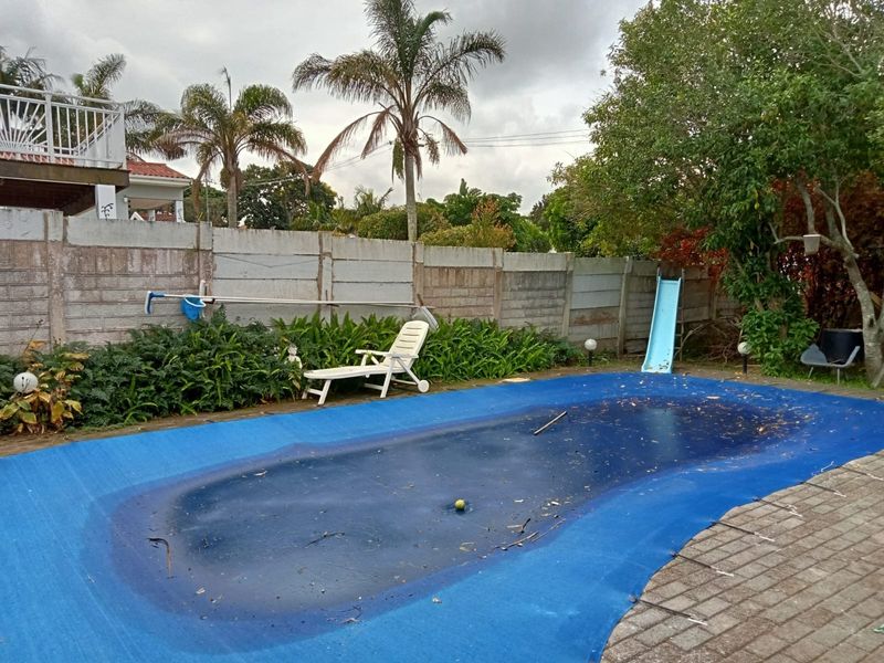 Outdoor pool area featuring a paved surround and a precast concrete boundary wall, currently requiring maintenance and cleaning.