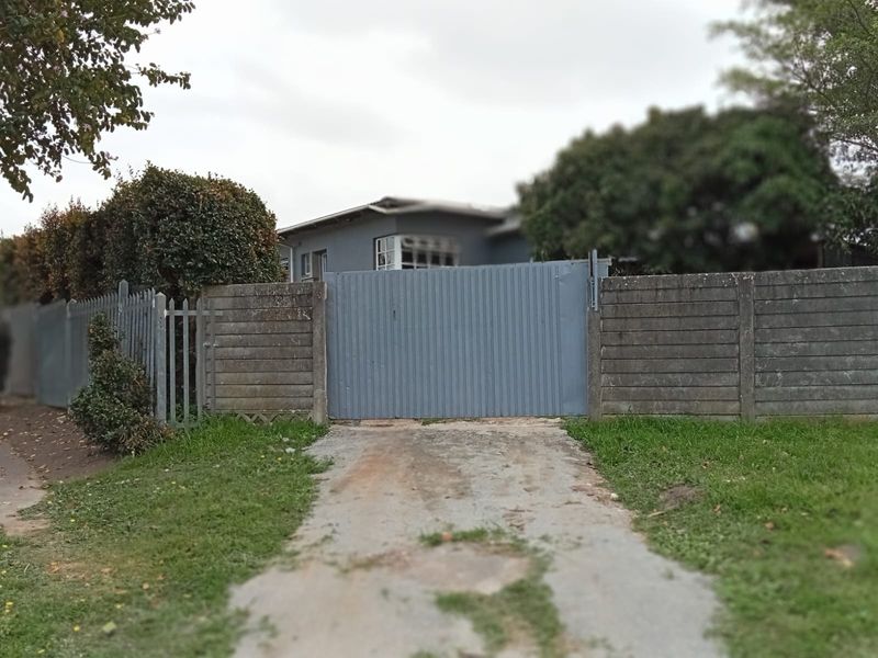 Front view of the property featuring a metal driveway gate, pedestrian gate, and concrete boundary wall with a paved driveway.