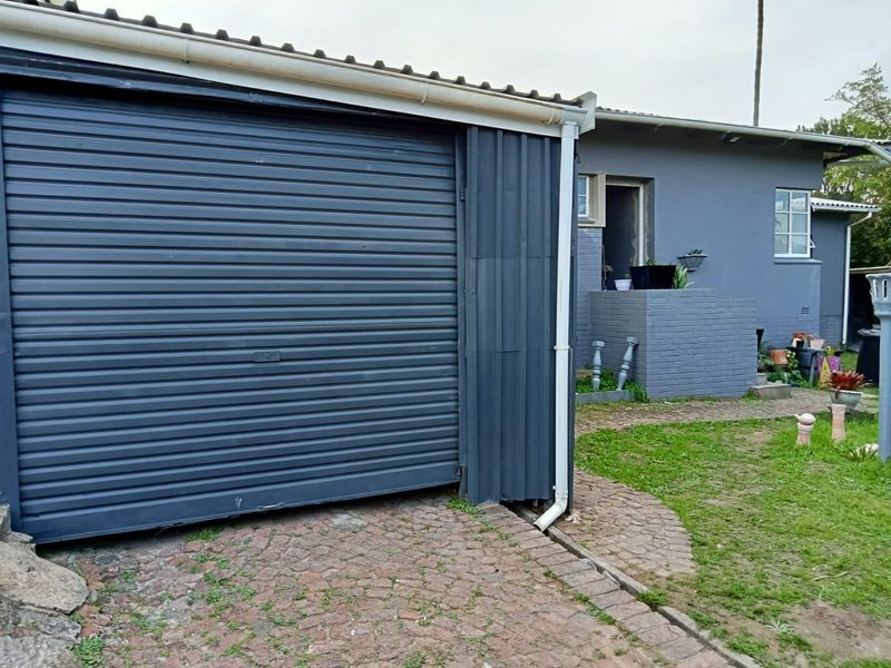 Exterior view of a residential property featuring a dark-painted roller shutter garage door, brick masonry walls, and a paved driveway area.