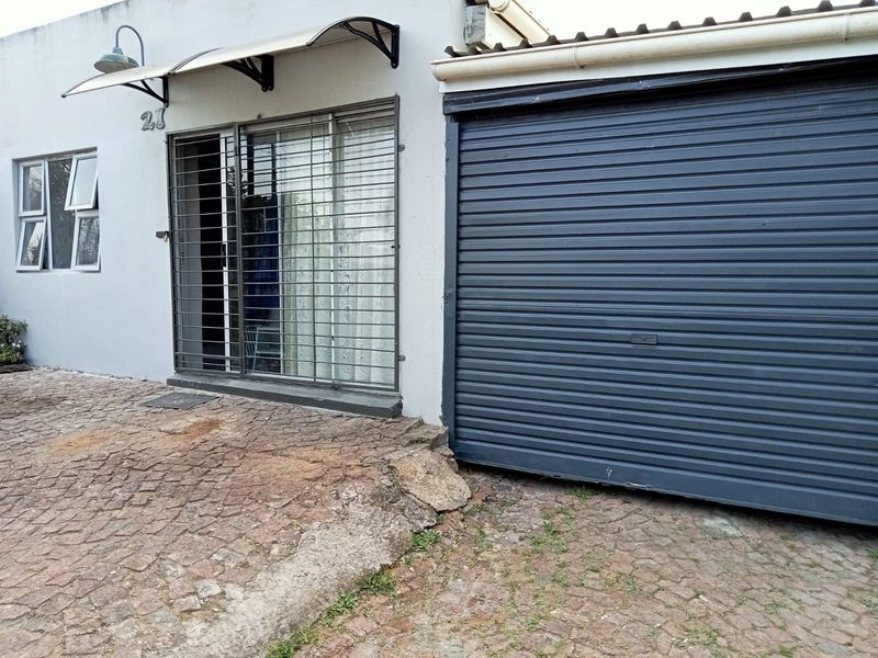 Front exterior view of the property featuring a roller garage door, security gate, and paved driveway area requiring maintenance.