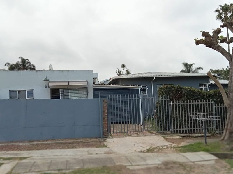 Front view of a residential property featuring a steel security gate, perimeter wall, and metal roofing with visible signs of exterior wear.