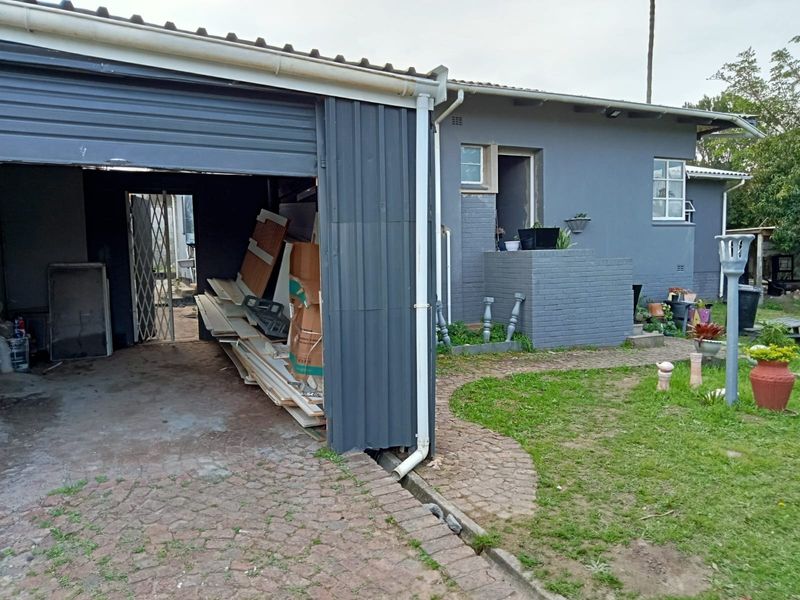Rear view of the property featuring a metal garage structure, brick masonry walls, and a paved walkway leading to the garden area.