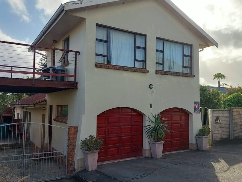 Front elevation of a two-story house featuring a double garage, a raised balcony with metal railings, and a paved driveway.