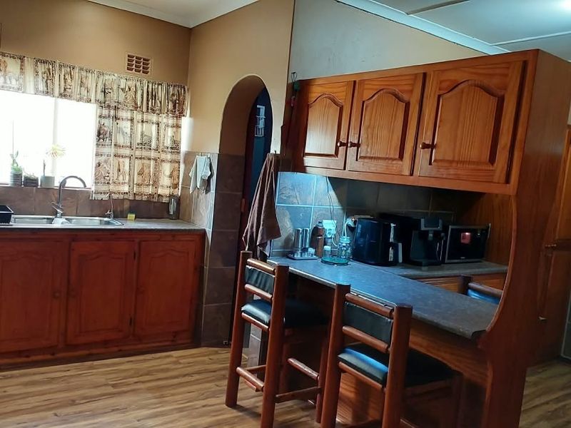 A functional kitchen featuring traditional wooden cabinetry, a breakfast bar, laminate countertops, and a double basin sink with a tiled backsplash.
