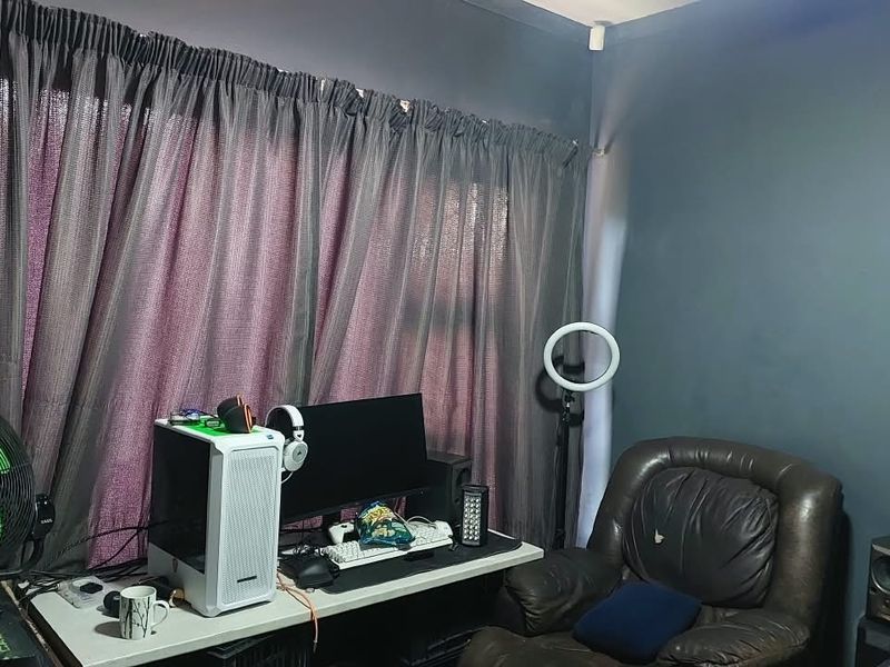 A bedroom space featuring dark grey walls and window curtain tracks, currently utilized as a home office and gaming area.