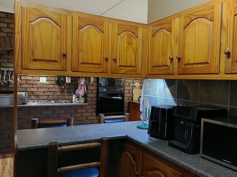 A rustic kitchen featuring traditional wooden cabinetry, exposed brick walls, and a functional breakfast bar layout with built-in oven and tiled backsplash.