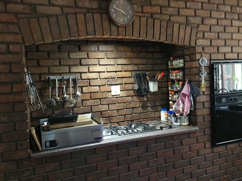 A rustic kitchen area featuring an exposed brick wall with a built-in gas hob, stone countertop, and integrated oven set within a brick archway.