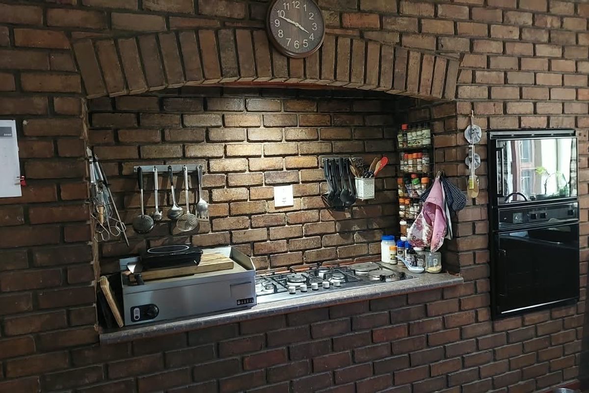A rustic kitchen area featuring an exposed brick wall with a built-in gas hob, stone countertop, and integrated oven set within a brick archway.