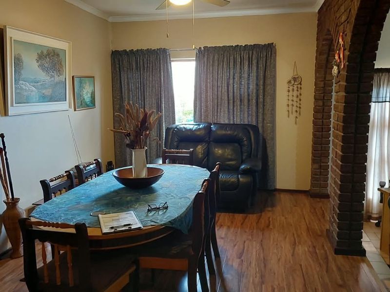 A dining room featuring laminate flooring, a brick archway, and a ceiling fan, offering a traditional layout with potential for modern updates.