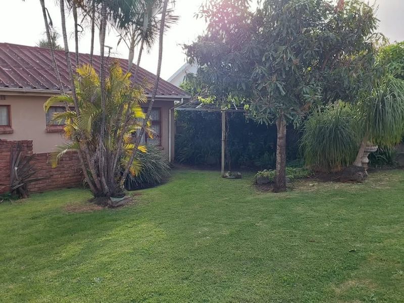 A view of the rear garden featuring a lawn, mature landscaping, and a brick retaining wall against the side of the house.