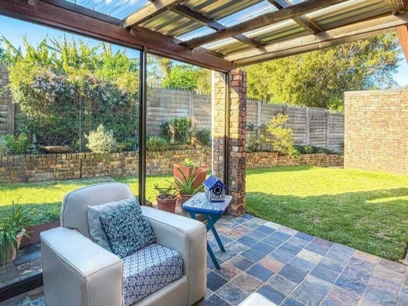 A covered patio area featuring slate tile flooring, a timber pergola structure, and direct access to a private rear garden with boundary walls.