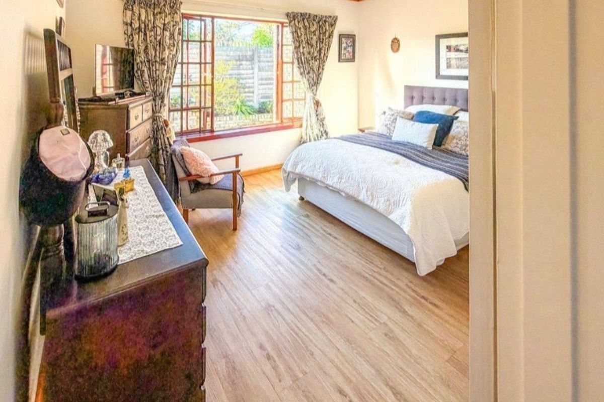A well-lit bedroom featuring light-toned laminate flooring and a large window with timber frames, offering a view of the rear garden area.
