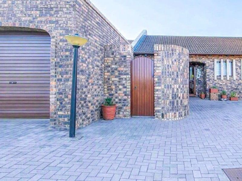 Front exterior view of a townhouse featuring a face brick facade, paved driveway, integrated garage with roller door, and a private pedestrian entrance.