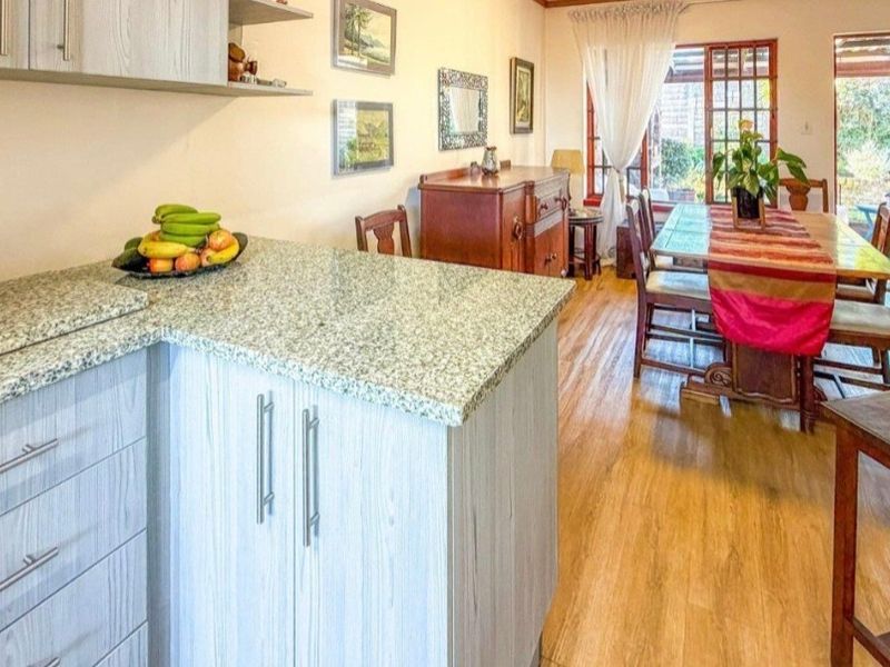 Open plan kitchen and dining area featuring granite countertops, light wood-look cabinetry, and laminate flooring with direct access to the outdoor patio.