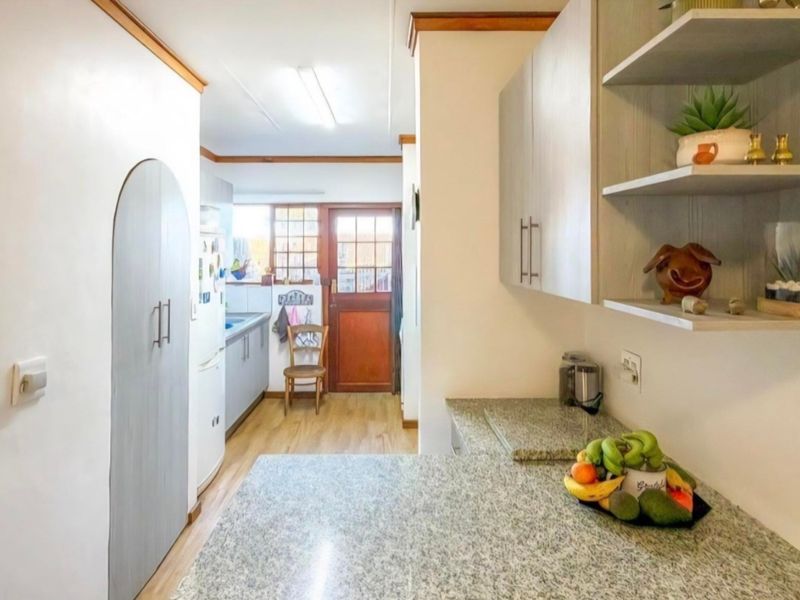 A functional kitchen featuring granite countertops, built-in cabinetry, and open shelving, leading to an exterior door with natural light.