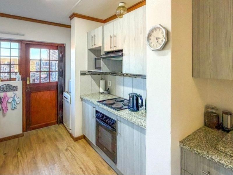 A functional kitchen featuring built-in cabinetry, granite countertops, an electric hob, and an oven, with direct access to the exterior via a wooden door.