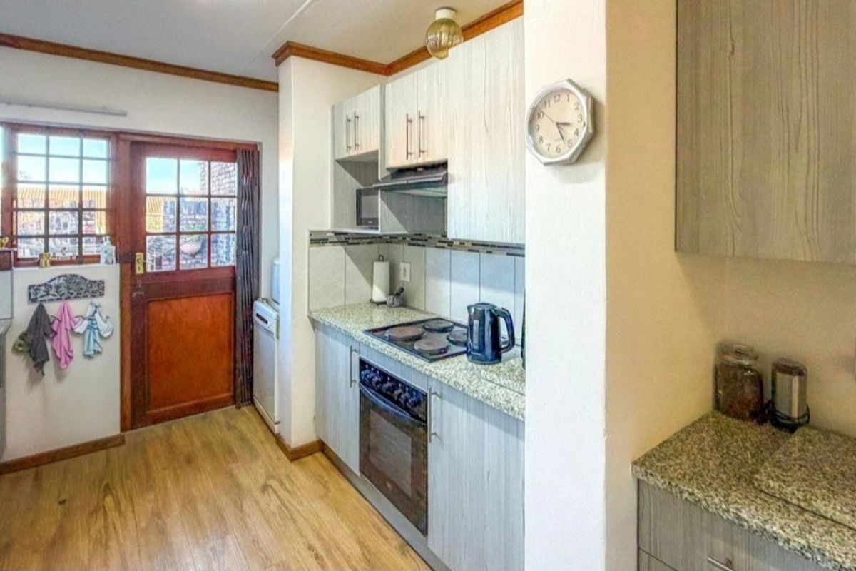 A functional kitchen featuring built-in cabinetry, granite countertops, an electric hob, and an oven, with direct access to the exterior via a wooden door.