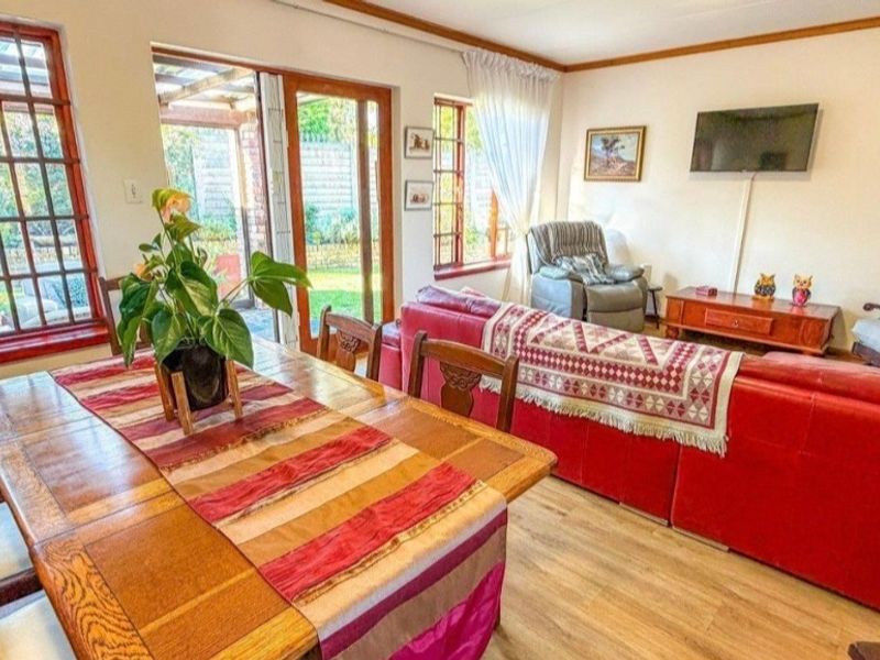 Open-plan living and dining area featuring laminate flooring, timber-framed windows, and sliding door access to the rear patio and garden.