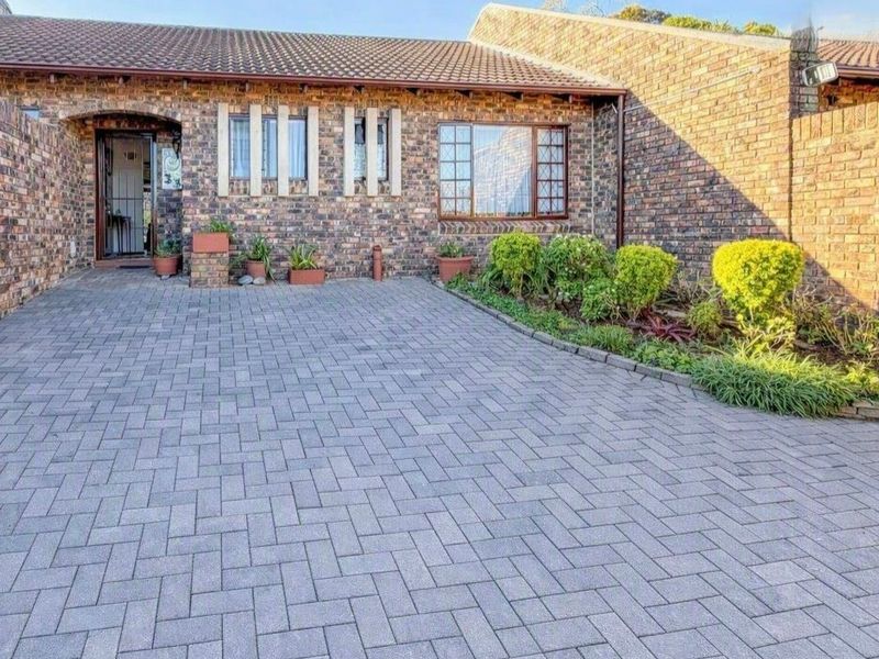 Front exterior view of a townhouse featuring a face brick facade, paved driveway, and a well-maintained garden bed.