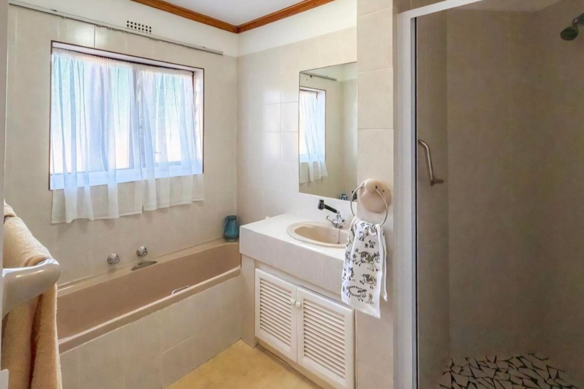 A functional bathroom featuring a built-in bathtub, a vanity unit with an integrated sink, and a separate shower enclosure with tiled finishes.