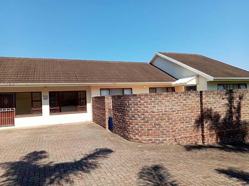 Front exterior view of the cluster home featuring a paved driveway, brick boundary wall, and tiled roof with secure access.