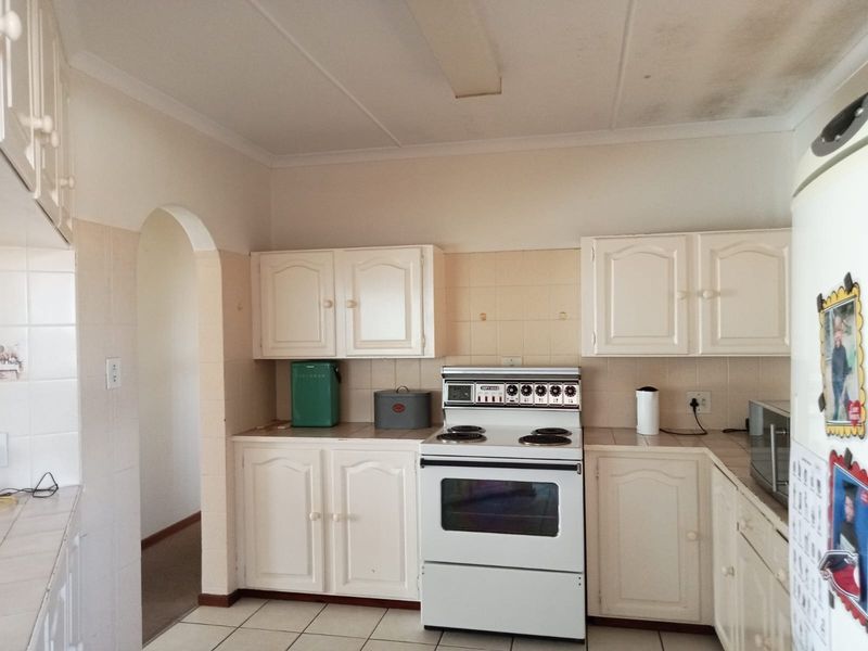 A dated kitchen featuring white cabinetry, tiled backsplash, and a freestanding electric stove, with visible ceiling water staining requiring attention.