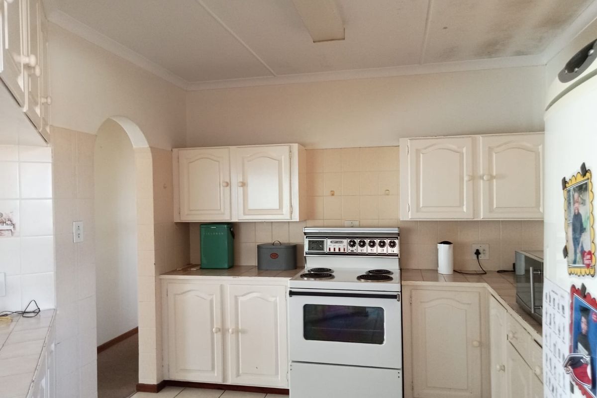 A dated kitchen featuring white cabinetry, tiled backsplash, and a freestanding electric stove, with visible ceiling water staining requiring attention.