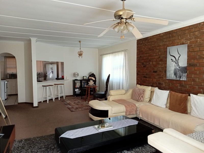 Open-plan living area featuring an exposed brick wall, ceiling fan, and a breakfast counter connecting to the kitchen space.