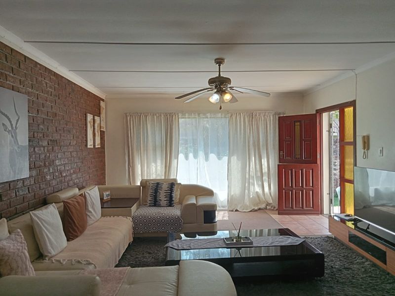 Spacious living room featuring an exposed brick accent wall, ceiling fan, and direct access to the exterior through a solid wood front door.