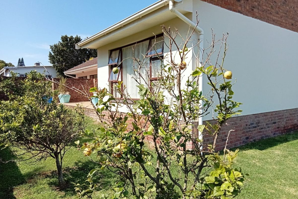 Rear exterior view of the property featuring a brick and plastered facade with aluminium window frames and established garden.
