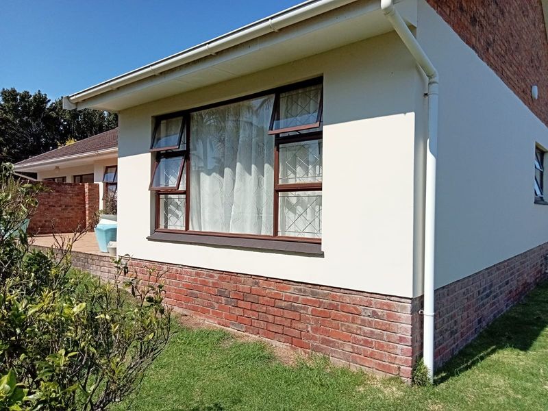 Rear exterior view of the property featuring a brick plinth, plastered walls, and aluminium window frames with integrated guttering and downpipe system.