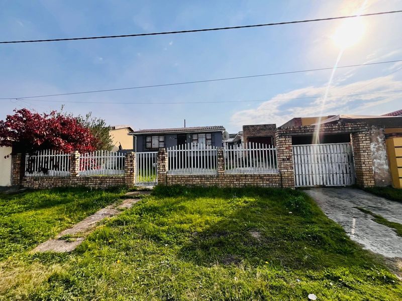 Front view of a residential property featuring a brick boundary wall, metal fencing, a driveway gate, and a paved driveway leading to the house.
