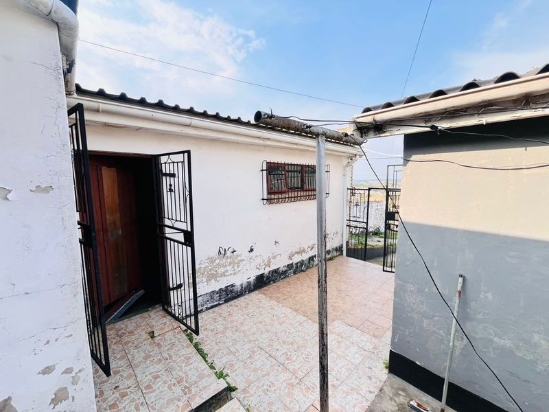 Rear exterior area featuring a tiled patio, security gates, and window bars, showing signs of significant wear and requiring maintenance.