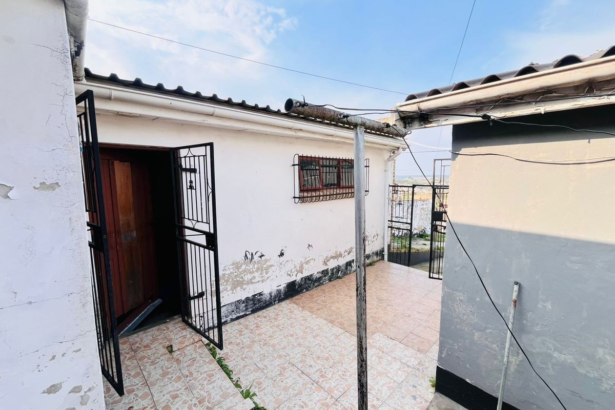 Rear exterior area featuring a tiled patio, security gates, and window bars, showing signs of significant wear and requiring maintenance.