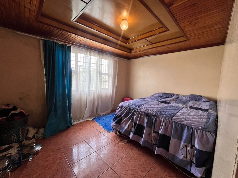 A bedroom featuring tiled flooring and a timber-paneled ceiling with a central light fixture.