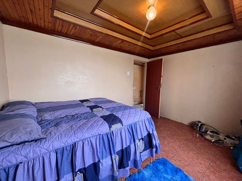 A bedroom featuring a timber-paneled ceiling with recessed detailing and tiled flooring, requiring cosmetic updates to improve the overall finish.