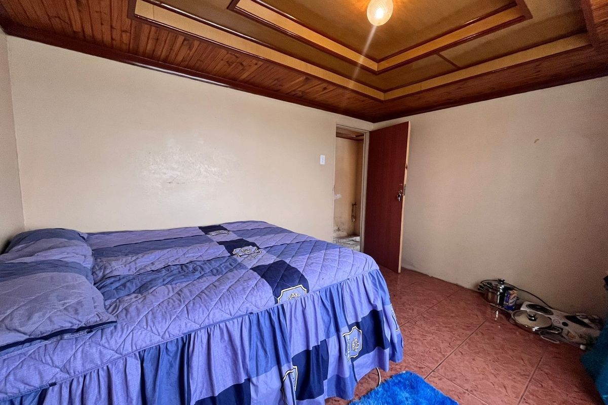 A bedroom featuring a timber-paneled ceiling with recessed detailing and tiled flooring, requiring cosmetic updates to improve the overall finish.