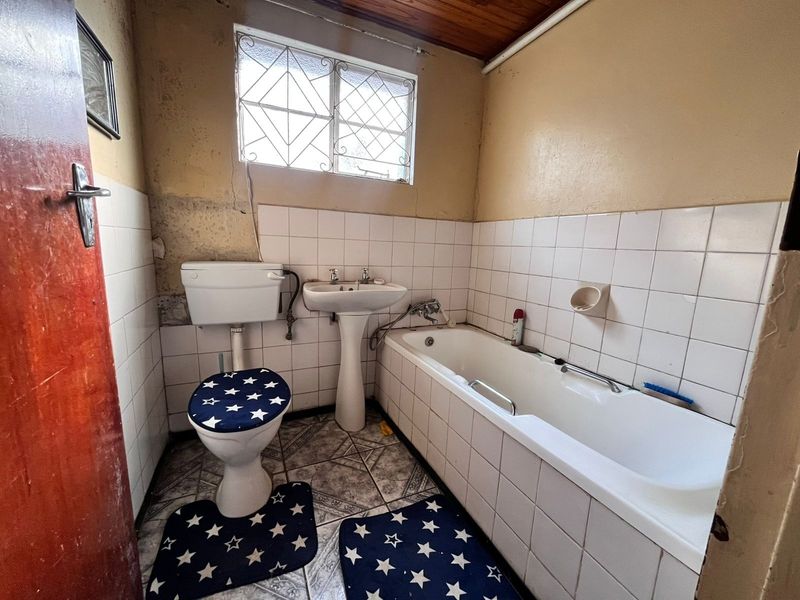 A dated bathroom featuring a pedestal basin, bathtub, and toilet, with tiled finishes and a timber ceiling, requiring significant renovation and cosmetic updates.