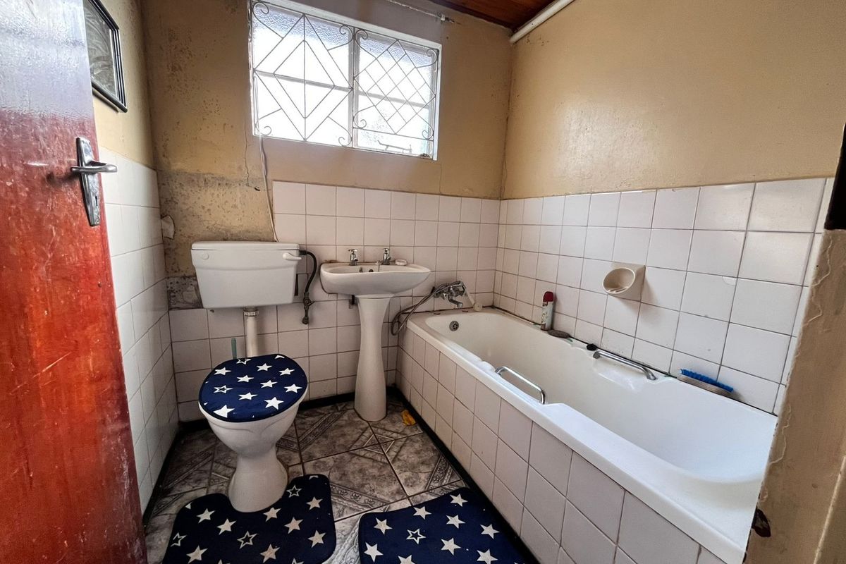 A dated bathroom featuring a pedestal basin, bathtub, and toilet, with tiled finishes and a timber ceiling, requiring significant renovation and cosmetic updates.