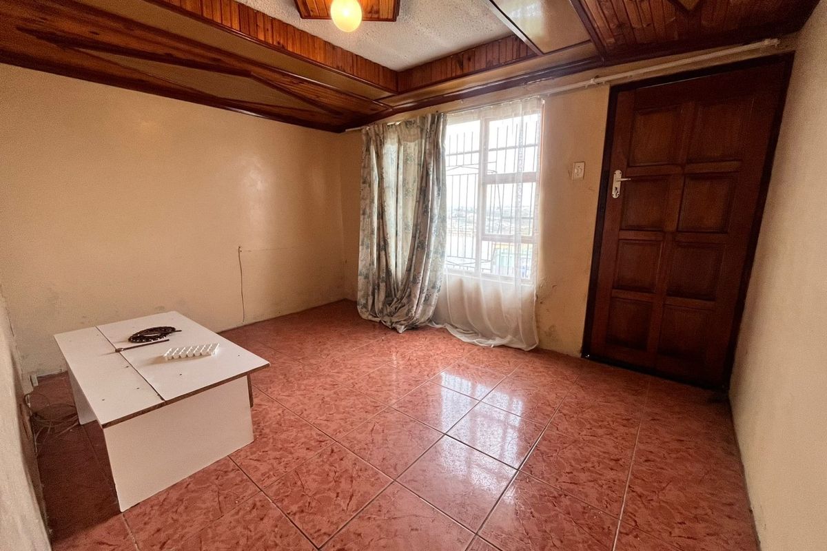 A vacant living room featuring timber ceiling beams, ceramic floor tiles, and a solid timber door, offering a blank canvas for renovation.