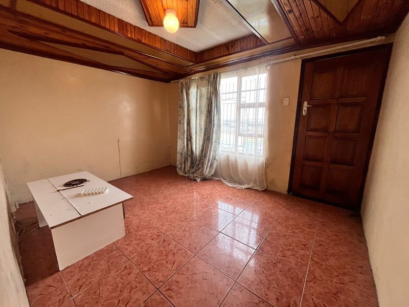 A vacant living room featuring timber ceiling beams, ceramic floor tiles, and a solid timber door, offering a blank canvas for renovation.